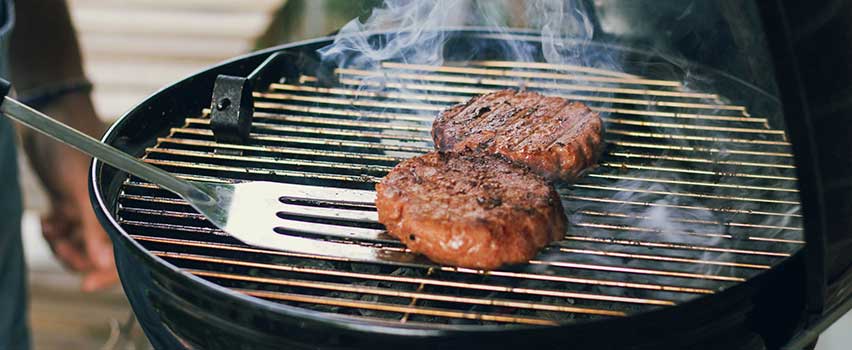 Grillbøffer steges over glødende kul på klassisk kulgrill med grillredskab i brug.