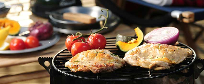 Saftige kyllingefileter og grøntsager tilberedes på gasgrill i udendørs sommermiljø.
