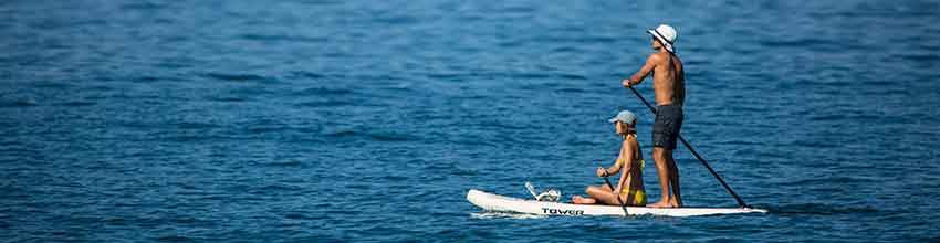 Mand og kvinde iført hat sejler på åbent hav på et hvidt paddleboard.