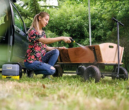 Kvinde spuler trævogn i haven med Kärcher mobil højtryksrenser til udendørs rengøring