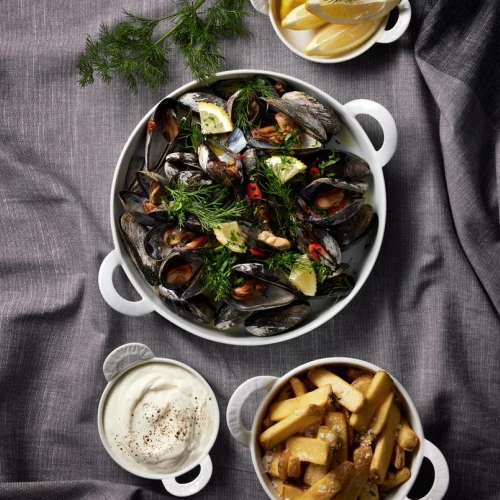 Ovnfast hvidt Pillivuyt fad med hanke fyldt med blåmuslinger og dild ved skåle med pommes frites og dip