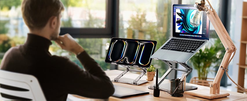 Mand arbejder ved skrivebord med laptop og tablet på Wozinsky justerbar stander i lyst kontor ved vindue