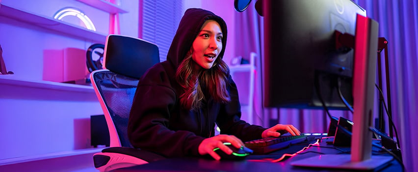 Ung kvinde gamer ved computer med Wozinsky gaming-mus og tastatur i mørkt rum med lilla RGB-belysning