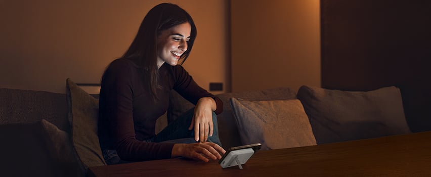 Kvinde smiler mens hun oplader smartphone trådløst med Wozinsky powerbank på bord i hyggeligt aftenslys