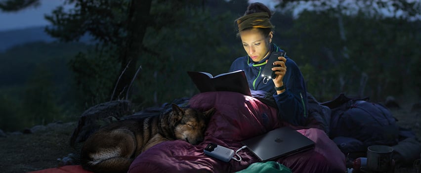 Kvinde læser bog i telt med hund og oplader smartphone og laptop med Wozinsky powerbank og pandelampe