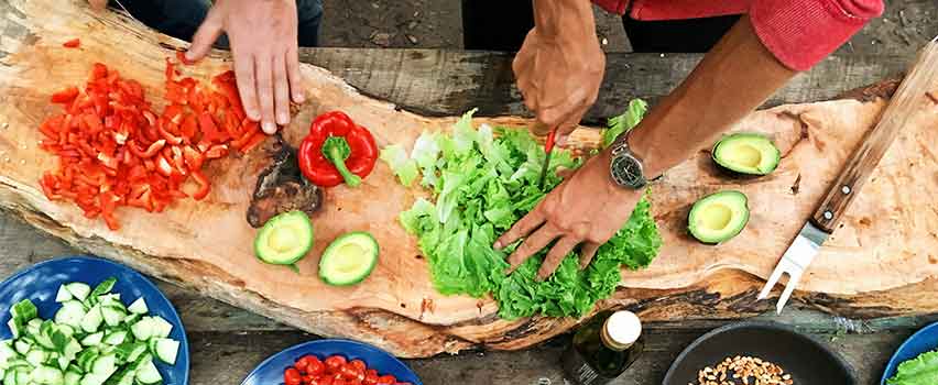 I et udendørskøkken bliver der skåret salat og rød peberfrugt.