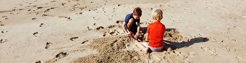 To børn bygger i sandet på strand, nyder sommerferie og udendørs leg ved havet.