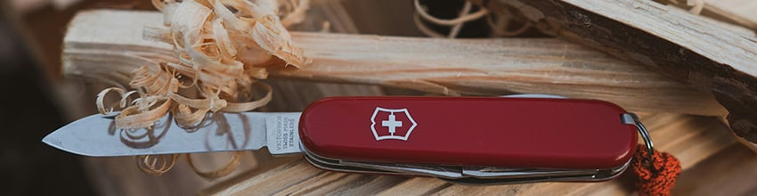 Rød Victorinox kniv ligger ovenpå stykker af træ og træskræller.