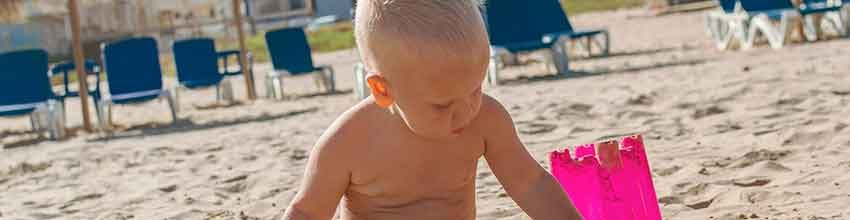 Barn leger i sandet på strand med spand i solen