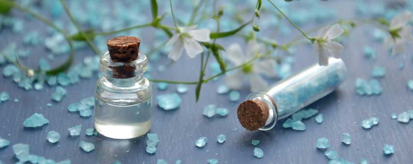 bord med mange små stykker glas, en hvid blomst på stilk og to små glas flasker med korkpropper